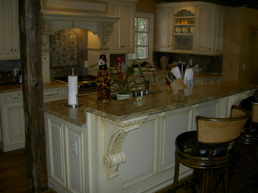 Example of a large mountain style l-shaped medium tone wood floor and brown floor open concept kitchen design with an undermount sink, white cabinets, granite countertops, brown backsplash, stone tile backsplash, stainless steel appliances and an island
