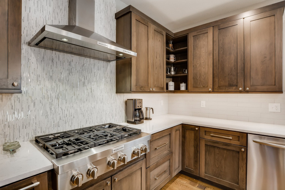 Photo of a large transitional u-shaped eat-in kitchen in Denver with a farmhouse sink, shaker cabinets, brown cabinets, quartz benchtops, white splashback, stainless steel appliances, medium hardwood floors, with island, brown floor and white benchtop.