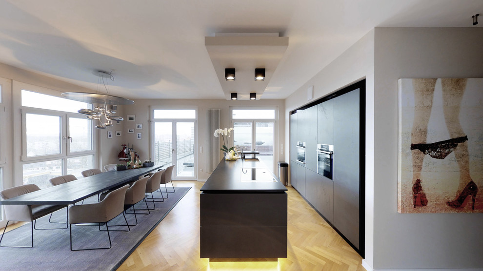 Photo of a large contemporary galley eat-in kitchen in Nuremberg with flat-panel cabinets, black cabinets, black appliances, medium hardwood floors, black benchtop, an undermount sink, with island and beige floor.