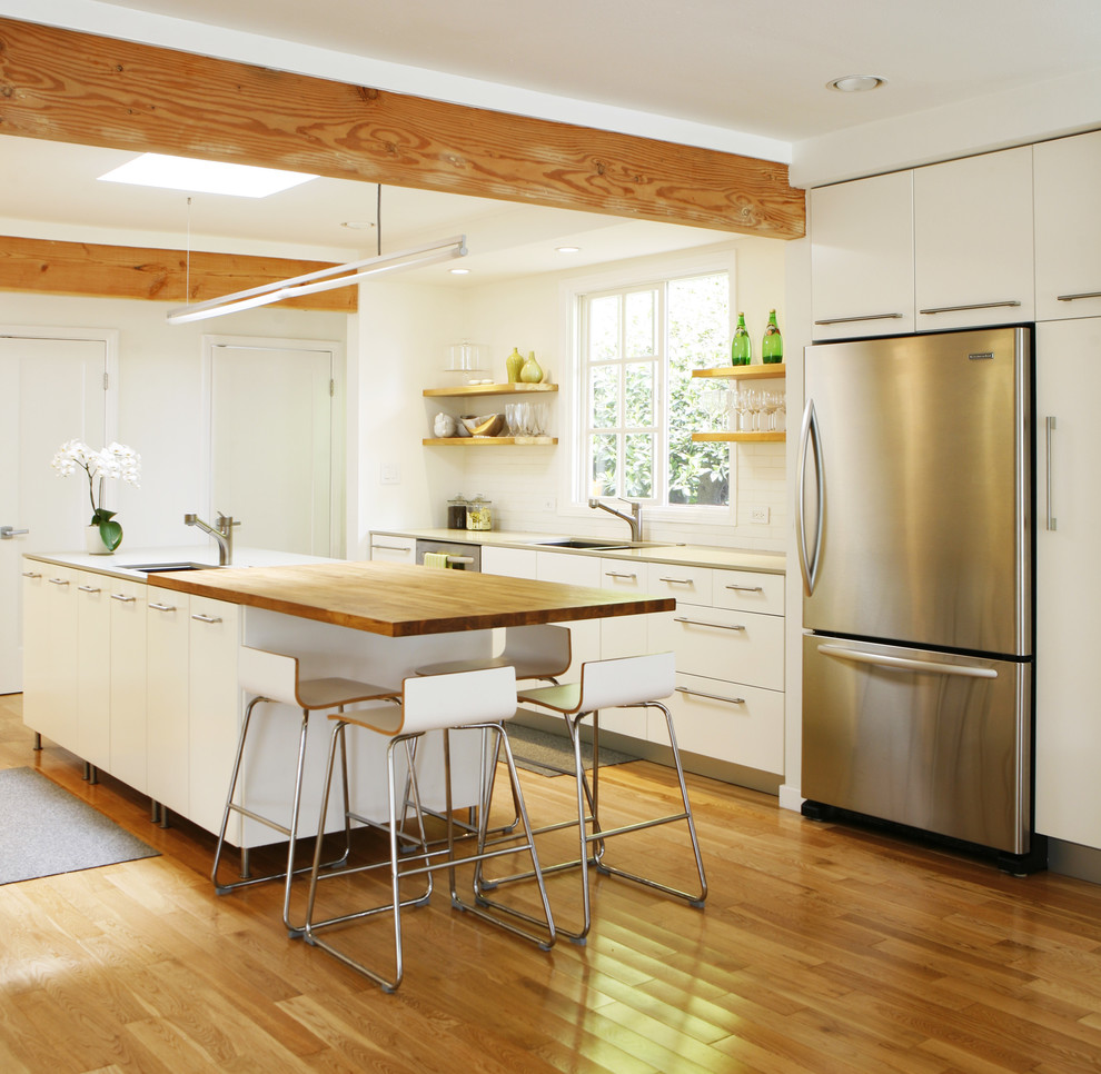 Design ideas for a modern kitchen in Los Angeles with stainless steel appliances, wood benchtops, flat-panel cabinets, white cabinets, white splashback, subway tile splashback, an undermount sink and with island.