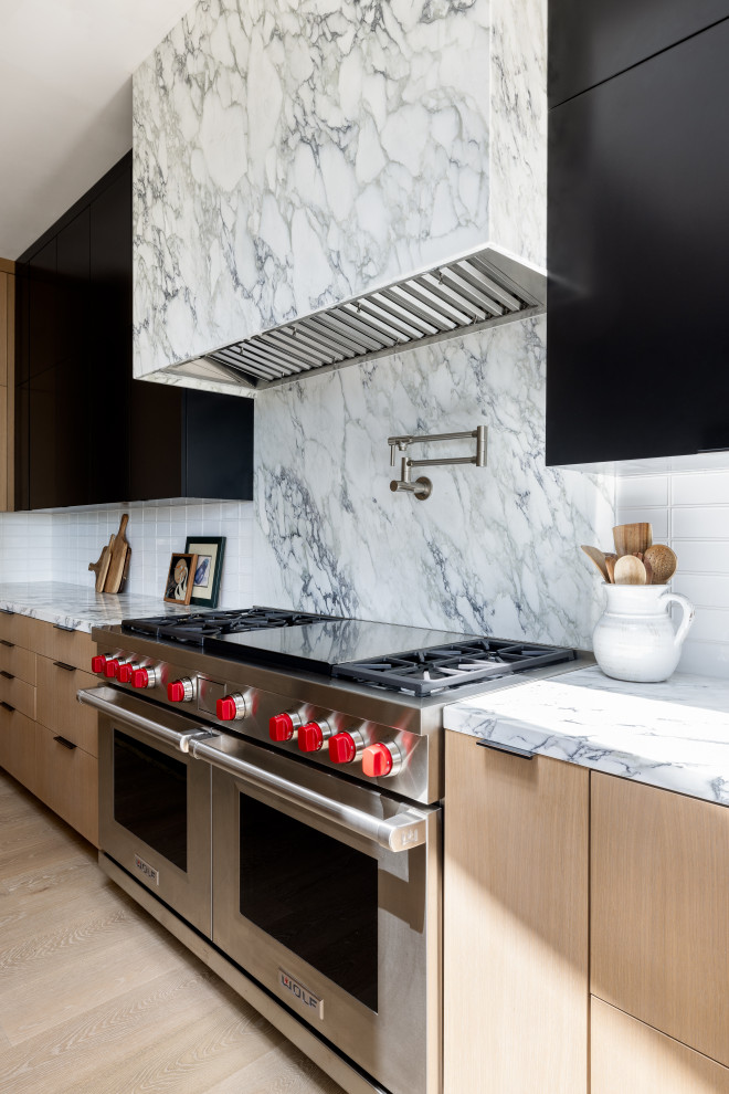 Design ideas for a large modern l-shaped kitchen/diner in Los Angeles with a built-in sink, flat-panel cabinets, black cabinets, soapstone worktops, white splashback, marble splashback, stainless steel appliances, medium hardwood flooring, an island, brown floors and black worktops.