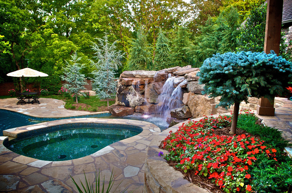 Large mediterranean custom-shaped natural pool in Oklahoma City with natural stone pavers and a hot tub.