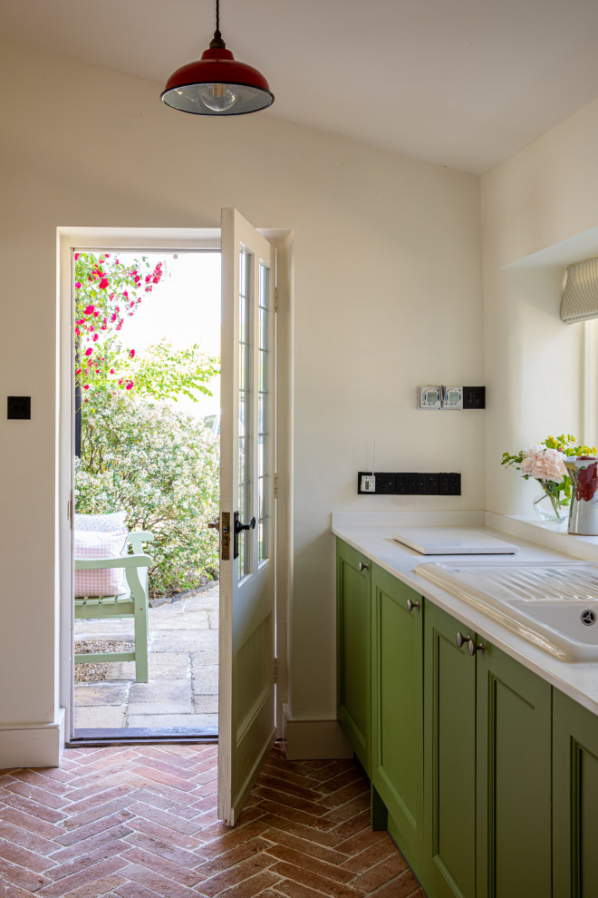 Mid-sized country single-wall utility room in Dorset with a single-bowl sink, shaker cabinets, quartzite benchtops, white walls, terra-cotta floors, a concealed washer and dryer, red floor and white benchtop.