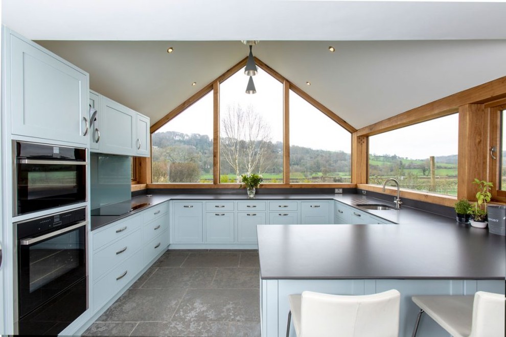Mid-sized transitional u-shaped open plan kitchen in Wiltshire with an integrated sink, shaker cabinets, blue cabinets, blue splashback, stainless steel appliances, no island and grey floor.
