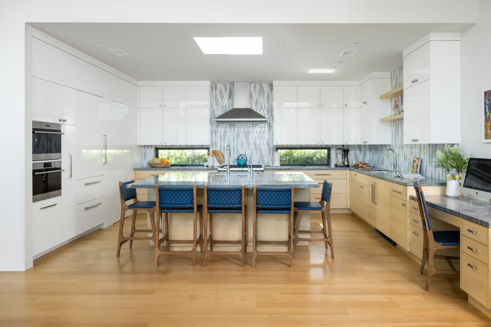 Exempel på ett stort modernt blå blått kök, med en undermonterad diskho, släta luckor, vita skåp, bänkskiva i kvartsit, flerfärgad stänkskydd, stänkskydd i keramik, integrerade vitvaror, ljust trägolv och en köksö