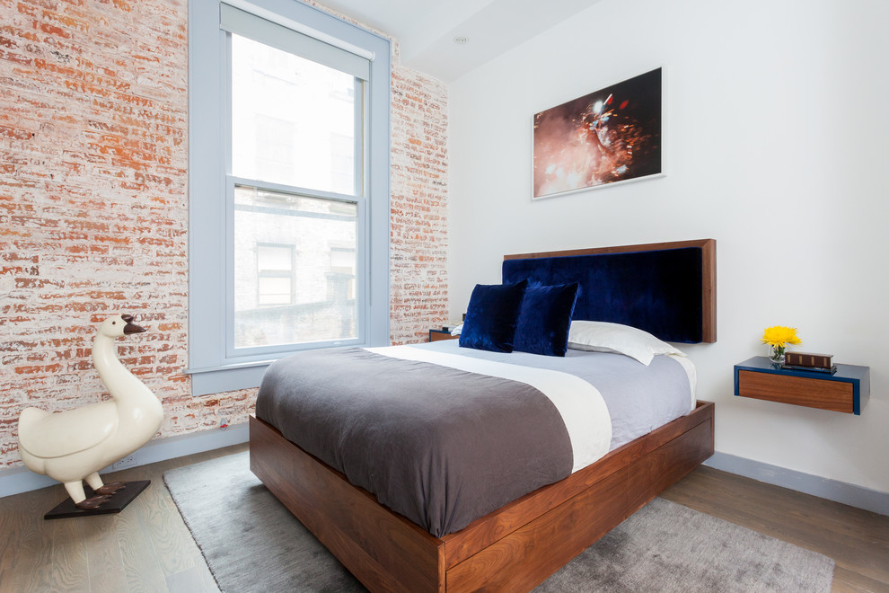 Small industrial master bedroom in New York with white walls and light hardwood floors.