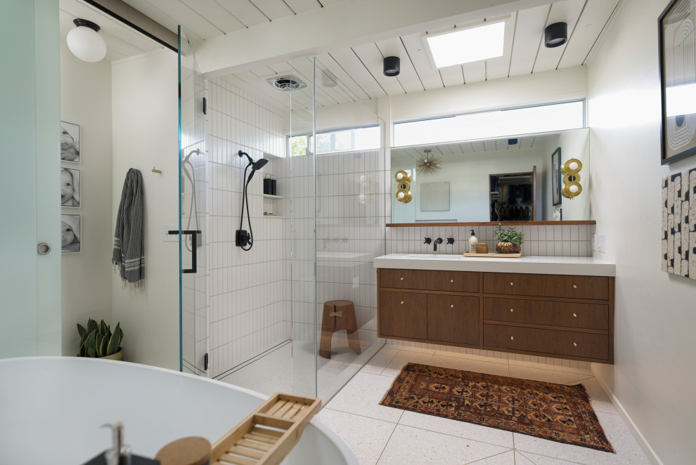 Стильный дизайн: главная ванная комната среднего размера в стиле ретро с плоскими фасадами, темными деревянными фасадами, отдельно стоящей ванной, угловым душем, раздельным унитазом, белой плиткой, керамической плиткой, белыми стенами, полом из терраццо, врезной раковиной, столешницей из искусственного кварца, бежевым полом, душем с распашными дверями, белой столешницей, нишей, тумбой под одну раковину, подвесной тумбой и деревянным потолком - последний тренд