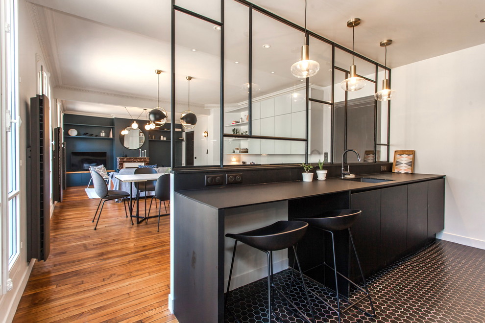 This is an example of a mid-sized contemporary single-wall open plan kitchen in Paris with an undermount sink, black cabinets, porcelain floors, with island, black floor, black benchtop and black splashback.