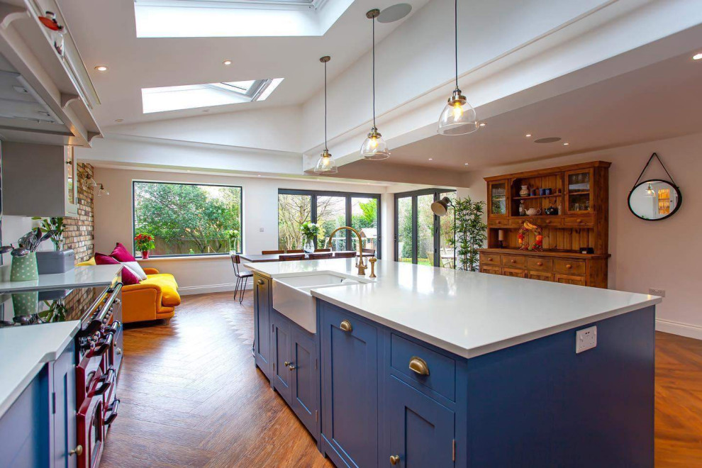 Mid-sized traditional l-shaped eat-in kitchen in Berkshire with a drop-in sink, shaker cabinets, blue cabinets, quartzite benchtops, green splashback, porcelain splashback, coloured appliances, vinyl floors, with island, brown floor and white benchtop.