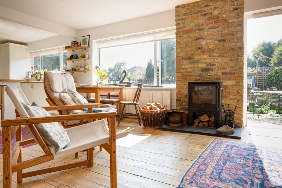 Example of a cottage medium tone wood floor and brown floor living room design in Surrey with white walls, a wood stove and a brick fireplace