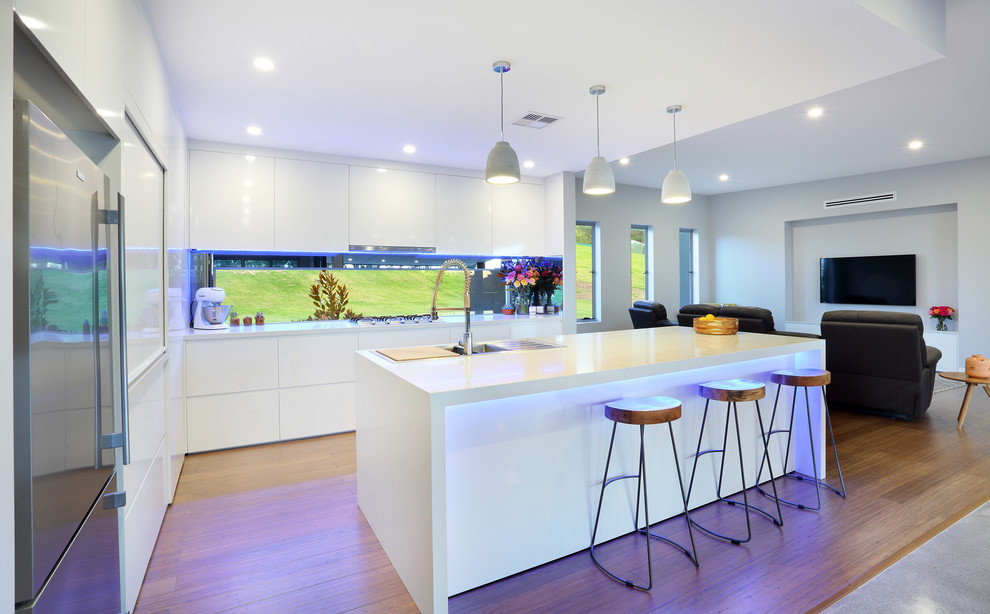 Design ideas for a mid-sized modern l-shaped kitchen in Sunshine Coast with a double-bowl sink, white cabinets, quartz benchtops, grey splashback, mirror splashback, stainless steel appliances, bamboo floors and with island.