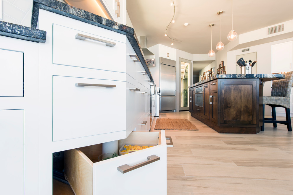 Photo of a mid-sized modern single-wall open plan kitchen in San Diego with a farmhouse sink, flat-panel cabinets, granite benchtops, grey splashback, subway tile splashback, stainless steel appliances, porcelain floors, with island and white cabinets.