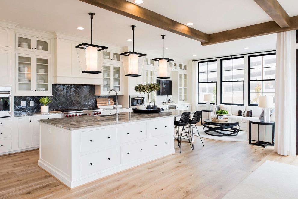 This is an example of a transitional galley open plan kitchen in DC Metro with glass-front cabinets, white cabinets, black splashback, light hardwood floors, with island and beige floor.