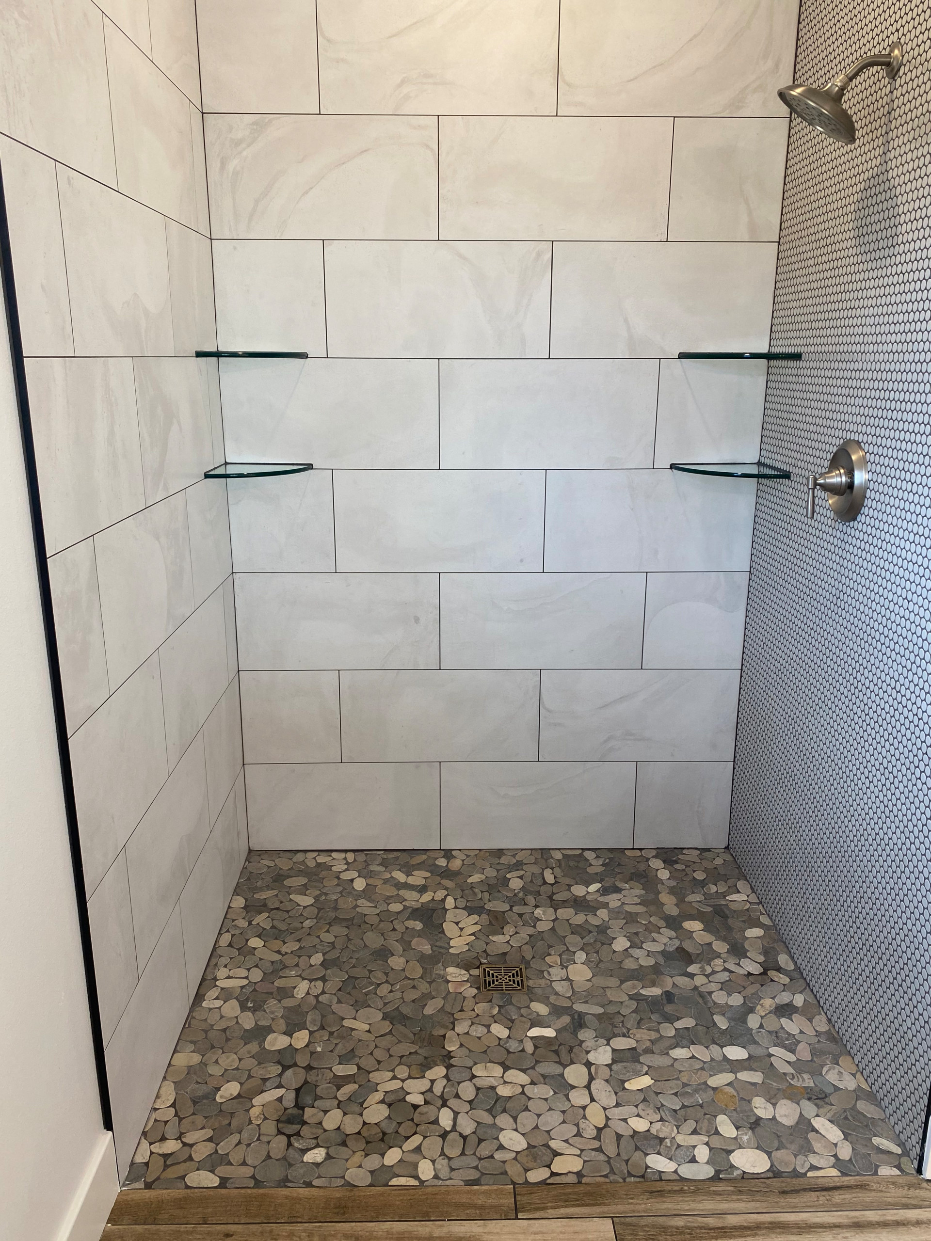 Custom tiled master shower with penny tile accent wall and rock floor