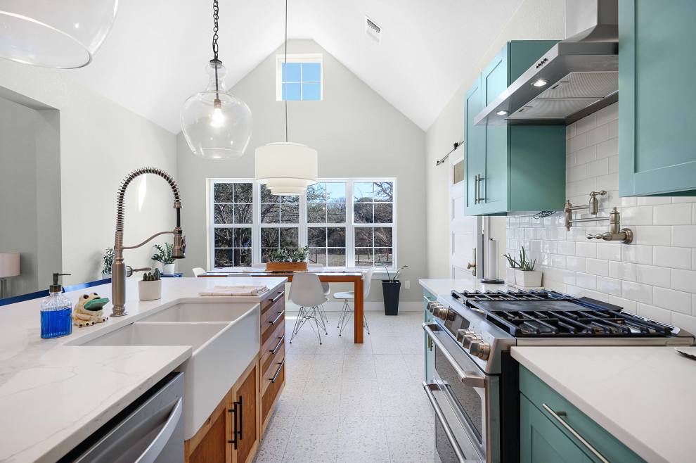 This is an example of a large country l-shaped open plan kitchen in Dallas with a farmhouse sink, flat-panel cabinets, blue cabinets, quartz benchtops, white splashback, ceramic splashback, stainless steel appliances, terrazzo floors, with island, white floor, white benchtop and vaulted.