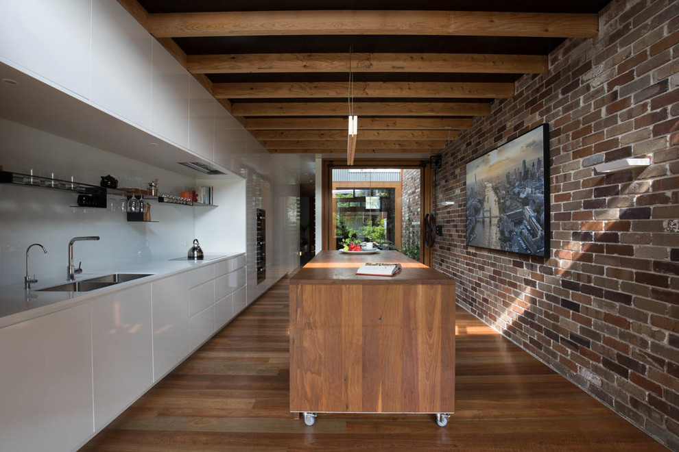 Contemporary single-wall eat-in kitchen in Sydney with a double-bowl sink, white splashback, black appliances, medium hardwood floors and with island.