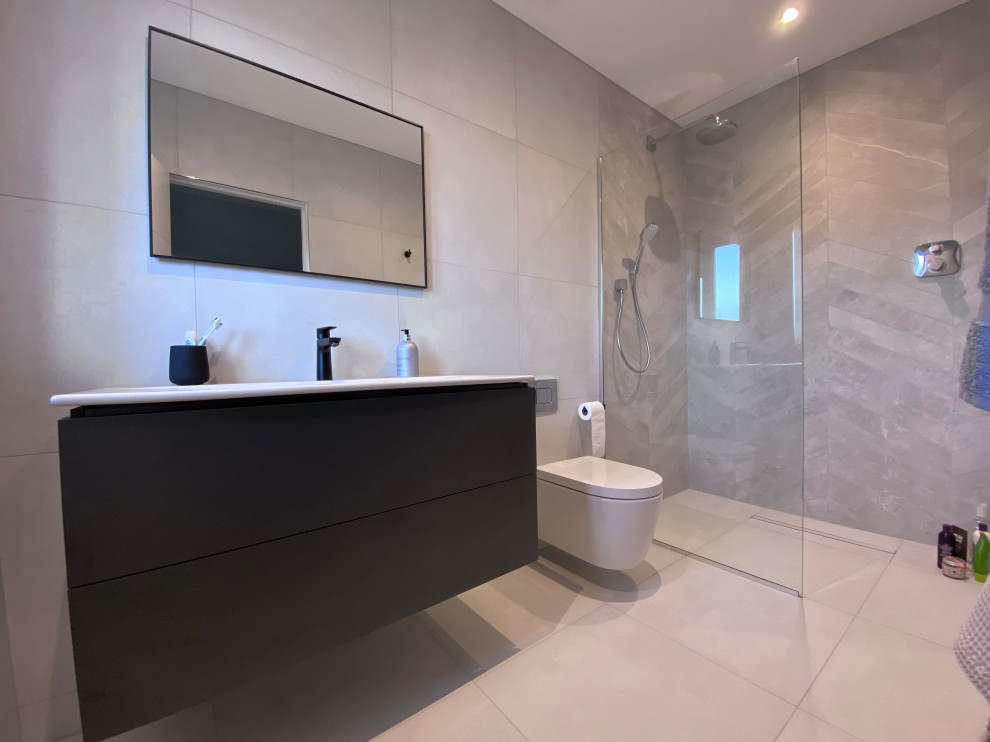 Idéer för att renovera ett mellanstort funkis vit vitt badrum med dusch, med släta luckor, svarta skåp, en öppen dusch, en vägghängd toalettstol, grå kakel, keramikplattor, grå väggar, klinkergolv i keramik, ett väggmonterat handfat, granitbänkskiva, grått golv och med dusch som är öppen