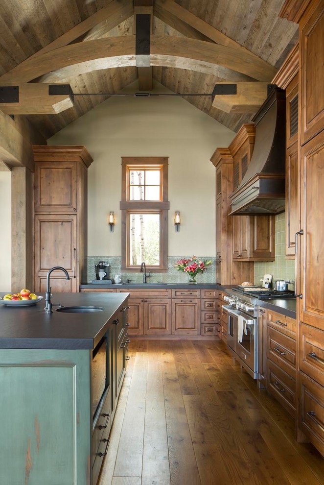 Inspiration for a large country l-shaped open plan kitchen in Denver with a single-bowl sink, raised-panel cabinets, green cabinets, granite benchtops, green splashback, ceramic splashback, panelled appliances, medium hardwood floors, with island, brown floor, black benchtop and wood.