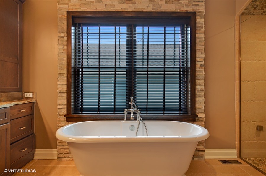 Design ideas for a large arts and crafts master bathroom in Chicago with shaker cabinets, dark wood cabinets, a freestanding tub, an alcove shower, a one-piece toilet, beige tile, stone tile, brown walls, porcelain floors, an undermount sink, granite benchtops, beige floor and a hinged shower door.