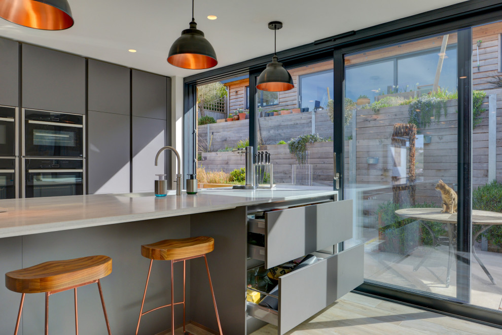 Immagine di un'ampia cucina minimalista con lavello integrato, ante lisce, ante grigie, top in superficie solida, elettrodomestici neri, parquet chiaro, pavimento marrone e top grigio