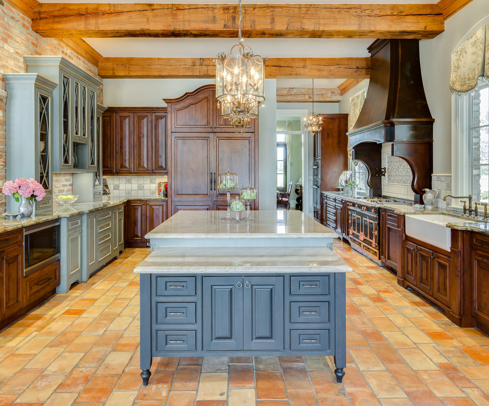 This is an example of an expansive traditional kitchen in New Orleans with a farmhouse sink, quartzite benchtops, terra-cotta floors, dark wood cabinets, multi-coloured splashback, black appliances, orange floor and multiple islands.