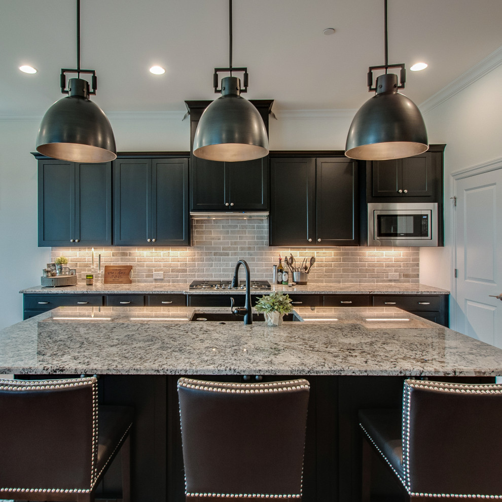 Photo of a mid-sized transitional eat-in kitchen in Nashville with an undermount sink, shaker cabinets, black cabinets, granite benchtops, grey splashback, limestone splashback, stainless steel appliances, medium hardwood floors, with island, brown floor and multi-coloured benchtop.