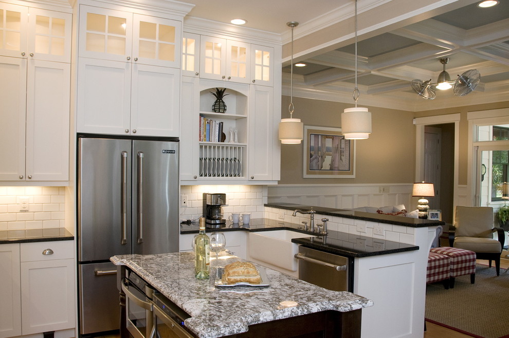 Photo of a beach style u-shaped open plan kitchen in Raleigh with stainless steel appliances, a farmhouse sink, recessed-panel cabinets, white cabinets, granite benchtops, white splashback and subway tile splashback.