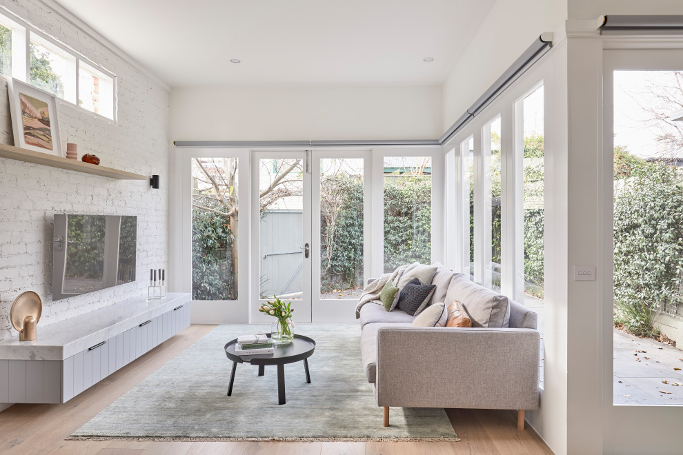 This is an example of a contemporary open concept living room in Melbourne with white walls, light hardwood floors, no fireplace, a wall-mounted tv and beige floor.