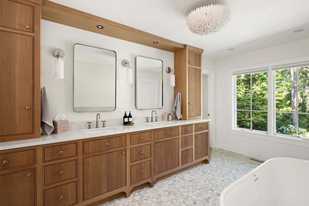 Example of a beach style pebble tile floor, gray floor and double-sink freestanding bathtub design in Minneapolis with beaded inset cabinets, medium tone wood cabinets, white walls, an undermount sink, white countertops and a built-in vanity