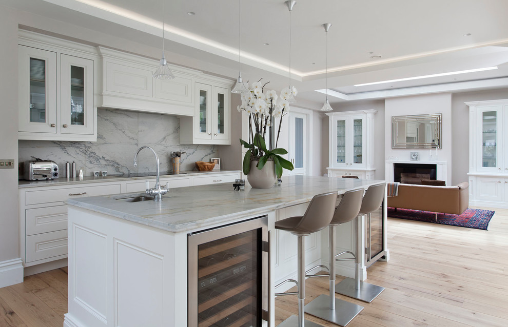 Photo of a large transitional galley open plan kitchen in Other with white cabinets, marble benchtops, white splashback, marble splashback, stainless steel appliances, light hardwood floors, with island, an undermount sink, recessed-panel cabinets, beige floor and white benchtop.