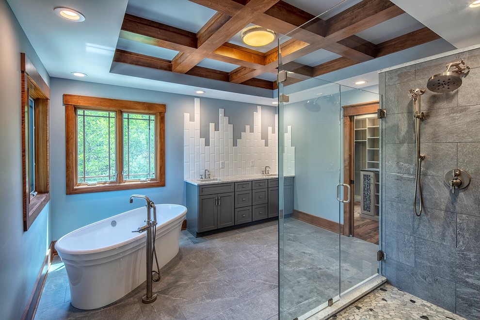 Photo of an arts and crafts bathroom in New York with recessed-panel cabinets, grey cabinets, a freestanding tub, a corner shower, gray tile, white tile, grey walls, an undermount sink, grey floor, a hinged shower door and white benchtops.