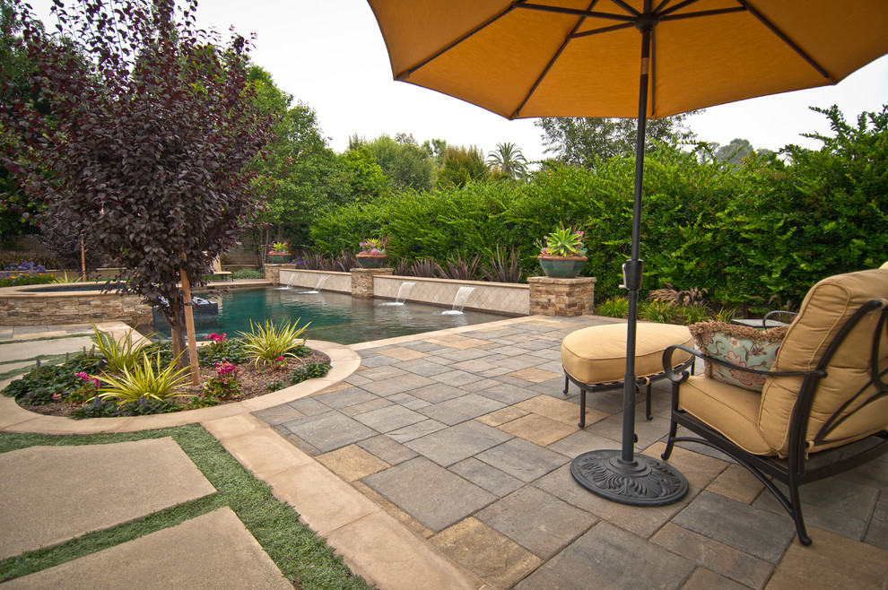 Large transitional backyard custom-shaped lap pool in Orange County with a hot tub and concrete pavers.