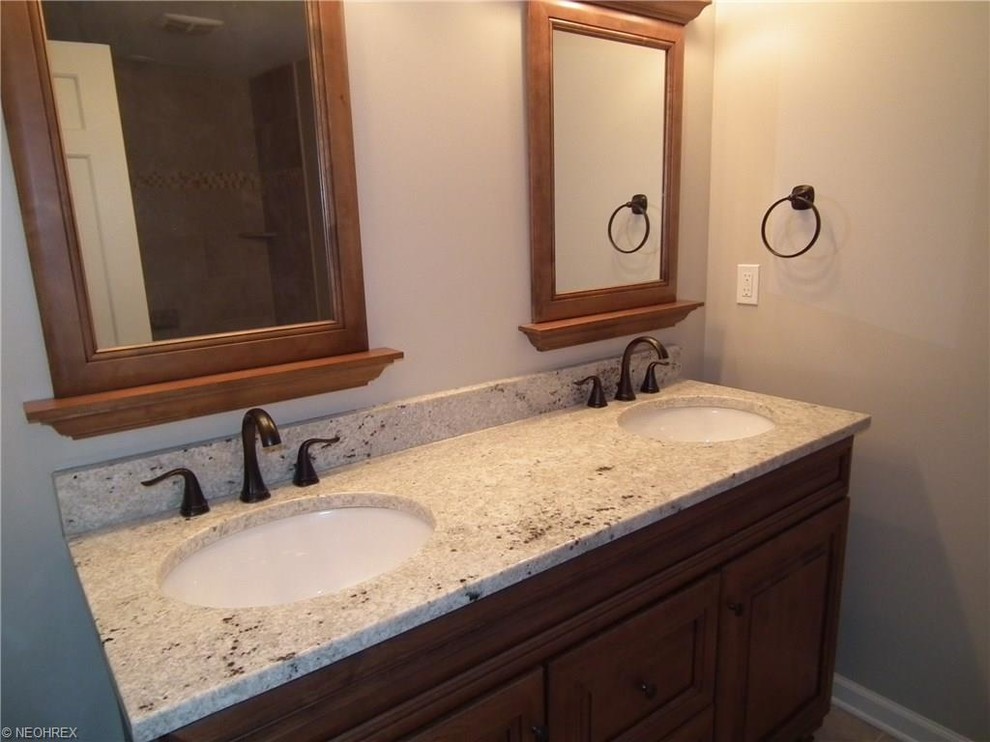 Mid-sized traditional bathroom in Cleveland with raised-panel cabinets, medium wood cabinets, granite benchtops, an alcove tub, a shower/bathtub combo, gray tile, porcelain tile and porcelain floors.