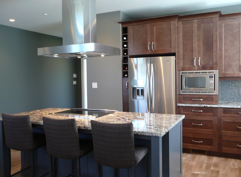 Photo of a contemporary l-shaped eat-in kitchen in Vancouver with an undermount sink, shaker cabinets, brown cabinets, granite benchtops, grey splashback, glass tile splashback and stainless steel appliances.