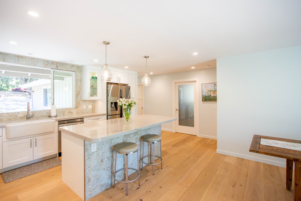 Eat-in kitchen - transitional l-shaped light wood floor and brown floor eat-in kitchen idea with a farmhouse sink, shaker cabinets, white cabinets, quartz countertops, porcelain backsplash, stainless steel appliances and an island