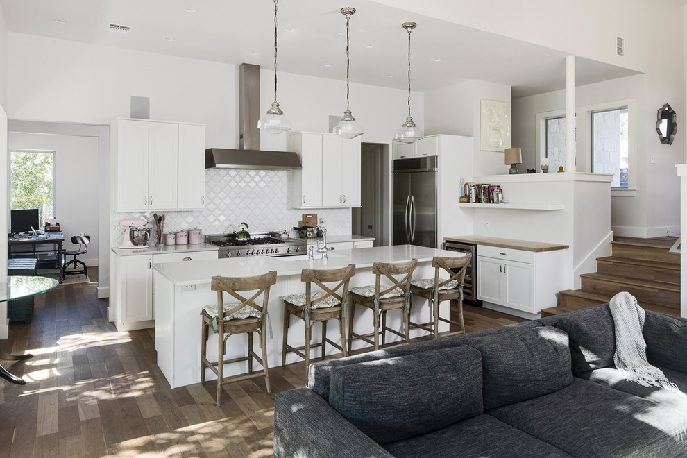 Design ideas for a mid-sized country l-shaped open plan kitchen in Austin with white cabinets, white splashback, ceramic splashback, stainless steel appliances, medium hardwood floors, with island, recessed-panel cabinets, quartz benchtops, brown floor and a farmhouse sink.