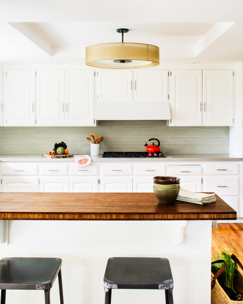 Photo of a large traditional kitchen in San Francisco with raised-panel cabinets, white cabinets, quartz benchtops, green splashback, glass tile splashback, medium hardwood floors and with island.