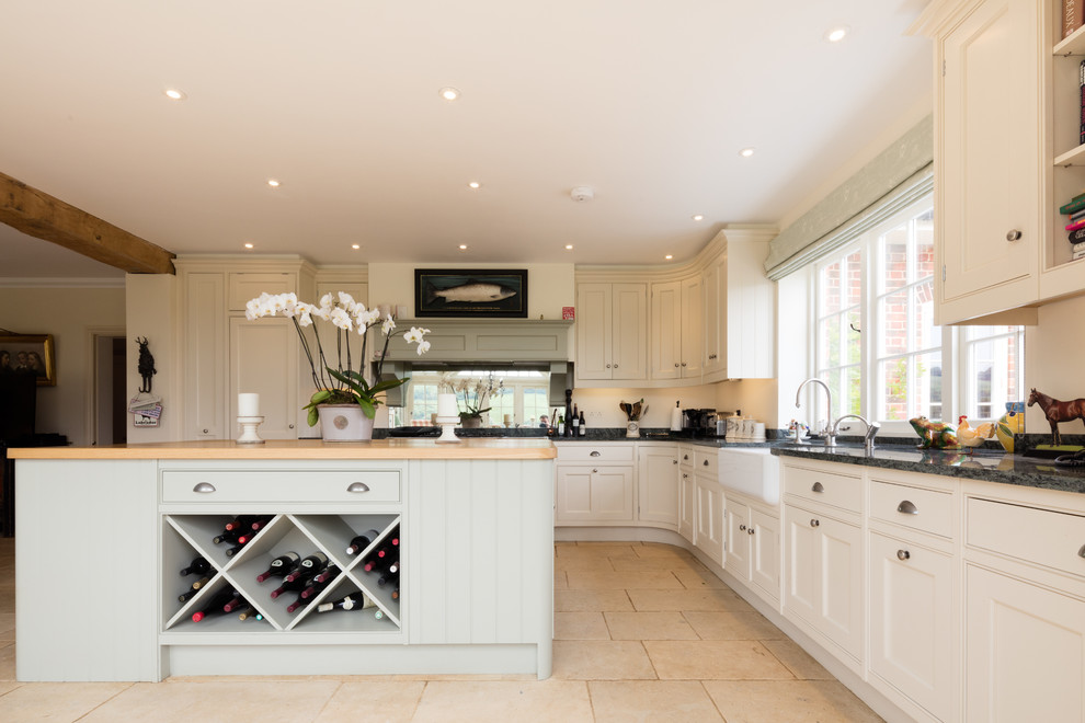 Traditional l-shaped kitchen in Wiltshire with a farmhouse sink, beaded inset cabinets, white cabinets, wood benchtops, mirror splashback, with island, beige floor and beige benchtop.