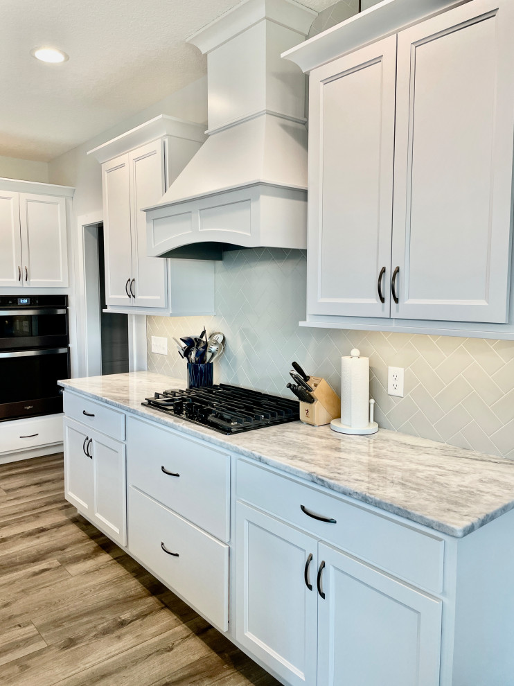 Large traditional l-shaped open plan kitchen in Other with a submerged sink, flat-panel cabinets, white cabinets, marble worktops, white splashback, metro tiled splashback, black appliances, an island and white worktops.
