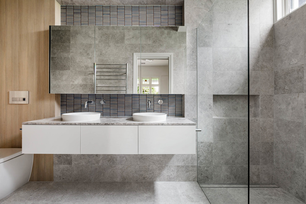 Inspiration for a contemporary bathroom in Melbourne with flat-panel cabinets, white cabinets, a double shower, a wall-mount toilet, gray tile, grey walls, a vessel sink, grey floor, an open shower and grey benchtops.