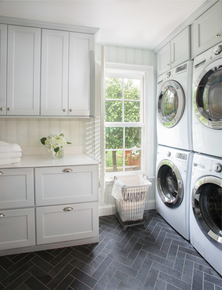Design ideas for a transitional l-shaped dedicated laundry room in St Louis with shaker cabinets, white cabinets, multi-coloured walls, a stacked washer and dryer, grey floor and white benchtop.