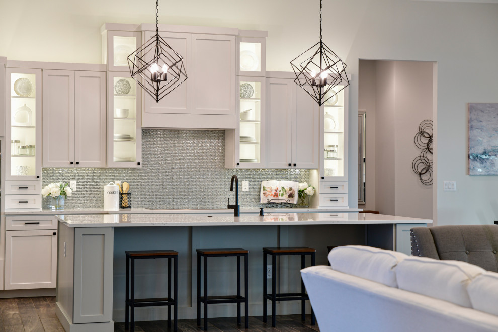 Inspiration for a mid-sized transitional l-shaped porcelain tile and brown floor eat-in kitchen remodel with a farmhouse sink, shaker cabinets, white cabinets, quartz countertops, metallic backsplash, glass tile backsplash, stainless steel appliances, an island and white countertops