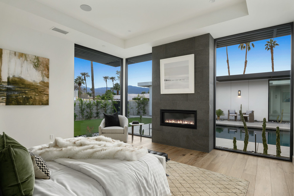 Contemporary bedroom in Los Angeles with white walls, light hardwood floors, a ribbon fireplace, a tile fireplace surround and beige floor.