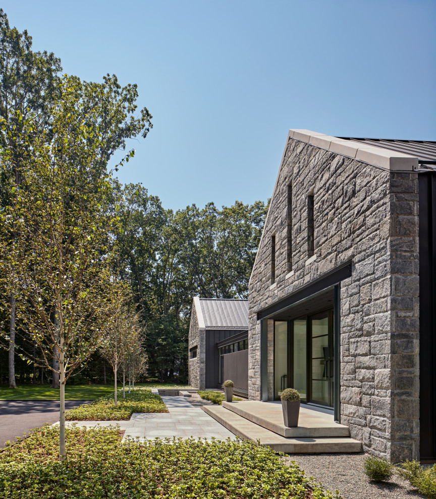 This is an example of a large contemporary two-storey grey house exterior in New York with stone veneer and a grey roof.