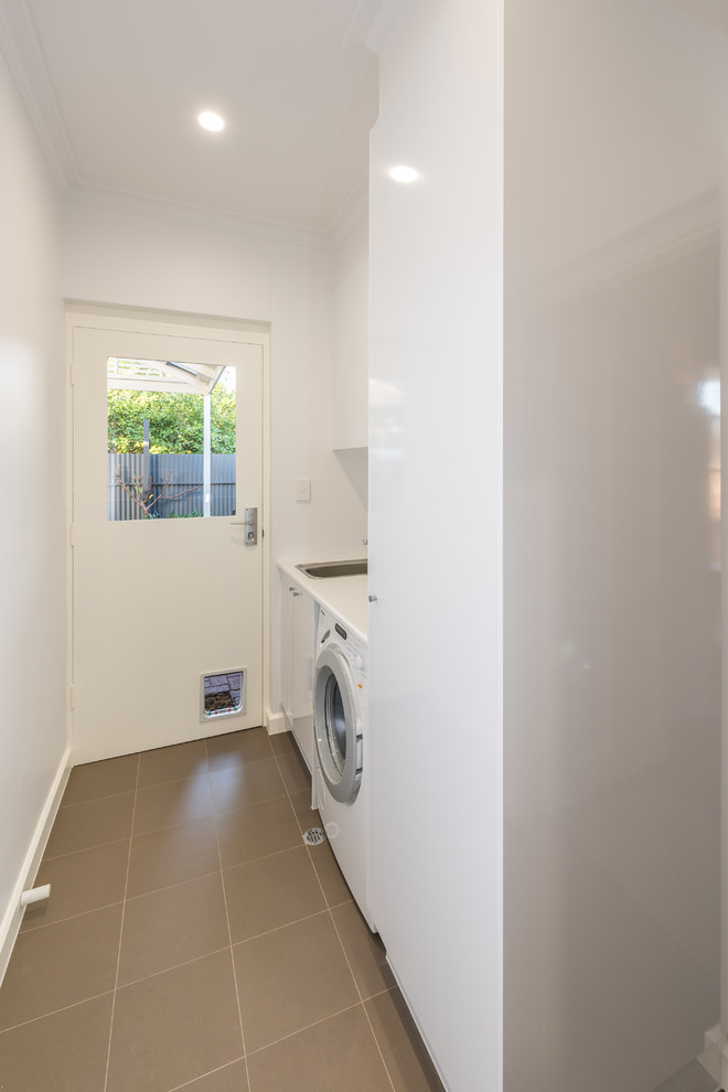This is an example of a small contemporary single-wall dedicated laundry room in Other with a single-bowl sink, white cabinets, laminate benchtops, white walls, ceramic floors and a side-by-side washer and dryer.