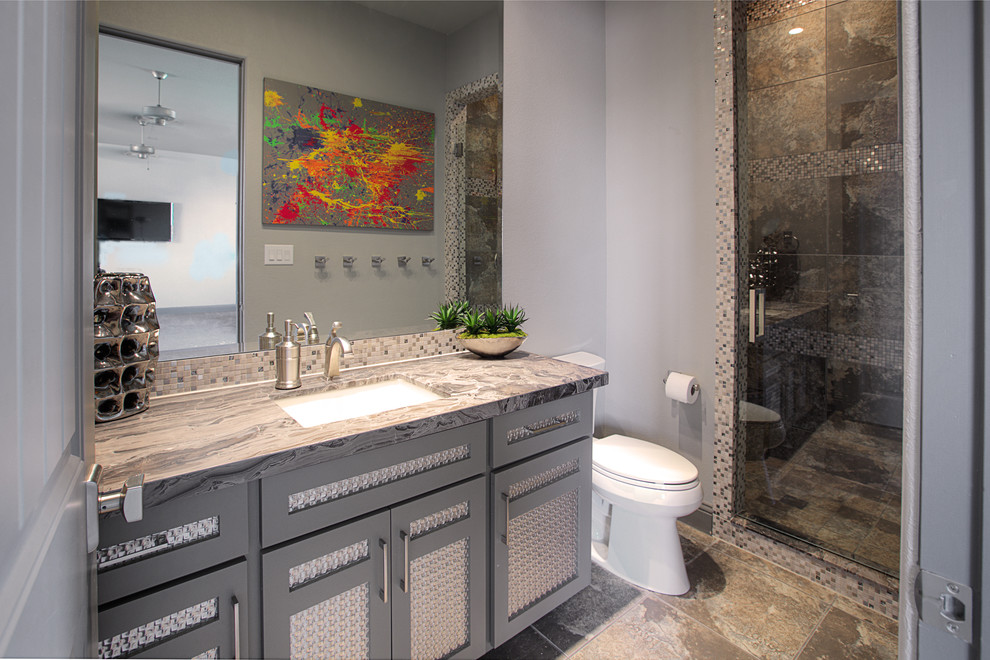 This is an example of a mediterranean 3/4 bathroom in Dallas with flat-panel cabinets, grey cabinets, an alcove shower, a one-piece toilet, gray tile, mosaic tile, grey walls, porcelain floors, an undermount sink, quartzite benchtops, grey floor, a hinged shower door and grey benchtops.
