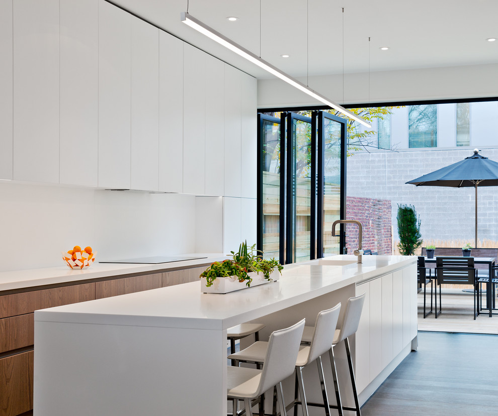 Photo of a mid-sized contemporary l-shaped eat-in kitchen in DC Metro with an integrated sink, flat-panel cabinets, white cabinets, quartz benchtops, white splashback, with island, panelled appliances, medium hardwood floors and white benchtop.