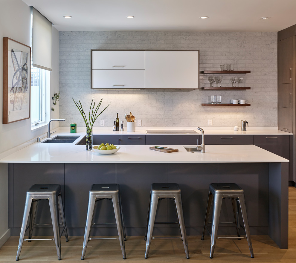 This is an example of a mid-sized modern u-shaped kitchen in San Francisco with an undermount sink, flat-panel cabinets, grey cabinets, grey splashback, medium hardwood floors, a peninsula, brown floor, quartz benchtops, marble splashback and white benchtop.
