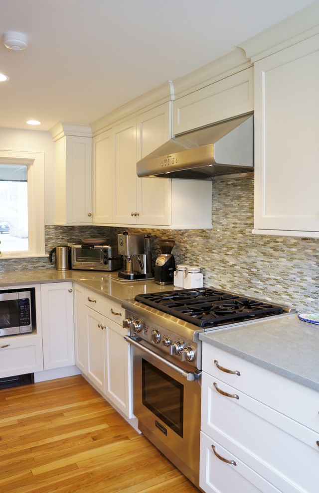 Eat-in kitchen - mid-sized transitional l-shaped light wood floor eat-in kitchen idea in Boston with a farmhouse sink, shaker cabinets, white cabinets, quartz countertops, blue backsplash, glass tile backsplash, paneled appliances and a peninsula