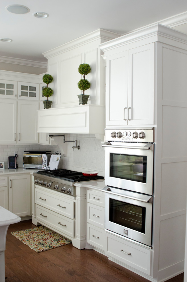 Inspiration for a mid-sized country l-shaped kitchen in Louisville with a farmhouse sink, white cabinets, quartz benchtops, white splashback, subway tile splashback, stainless steel appliances, medium hardwood floors, with island, brown floor, white benchtop and shaker cabinets.